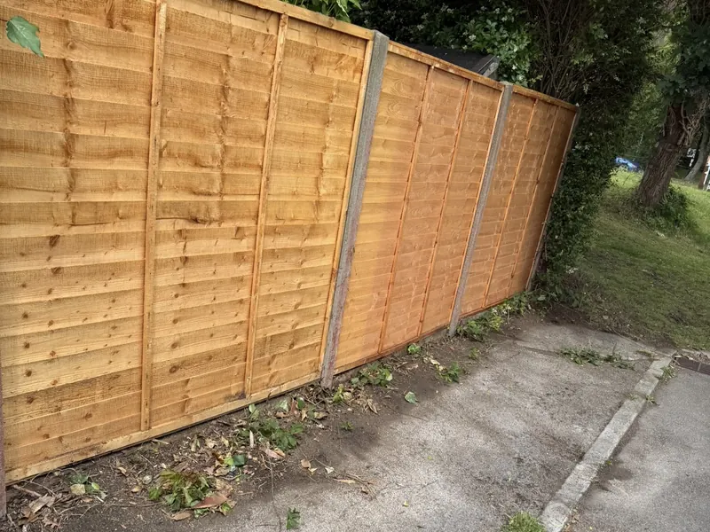 New lap fence panels between concrete posts beside a pavement
